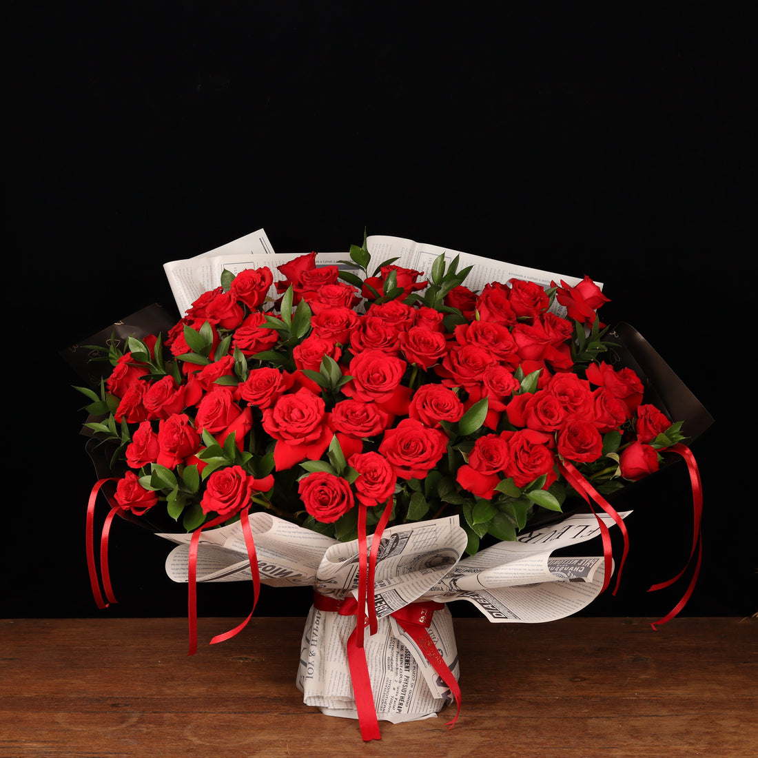 50 red roses with ruscus in newspaper-style paper, a Valentine's Day bouquet delivered in Dubai