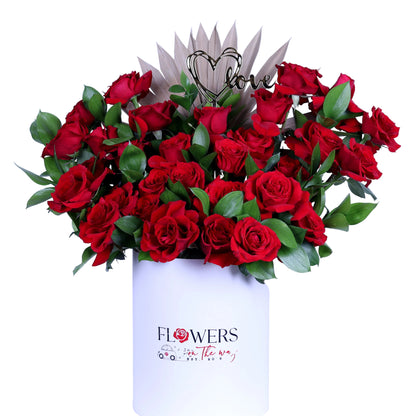 Delight your loved one with the “Pure Romance” Red Roses Arrangement, featuring vibrant red roses beautifully accented with fresh ruscus leaves and a charming acrylic heart, elegantly presented in a white round box. Perfect for Valentine’s Day, anniversaries, birthdays, or intimate romantic gestures, this luxurious bouquet conveys elegance, passion, and heartfelt emotion in every detail.