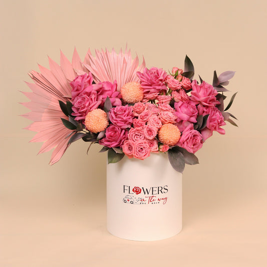 Bouquet of pink and peach flowers in a white container with 'FLOWERS' branding on a beige background