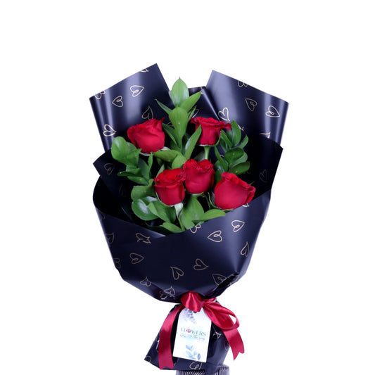 Make a lasting impression with the “Velvet Desire” Bouquet, featuring 5 fresh, vibrant red roses paired with lush ruscus leaves, elegantly wrapped in classic black paper. Perfect for Valentine’s Day, anniversaries, birthdays, or romantic gestures, this bouquet combines romance, elegance, and heartfelt emotion in a compact, luxurious design. A refined gift that expresses love with style and sophistication.